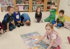 Dziewczynka przyczepia postać Nudka do plakatu.