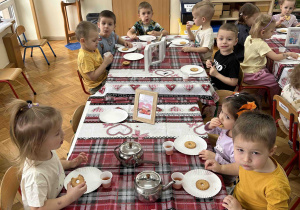Dzieci jedzą ciasteczka i piją herbatkę.