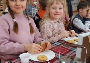 Uśmiechnięte dziewczynki zjadają ciasteczka.
