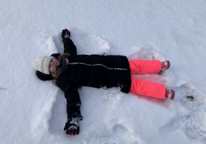 Dziewczynka leży na śniegu i robi aniołka.