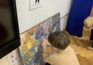 Chłopiec przykleja Nudka na plakacie projektu.