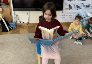 Dziewczynka prezentuje przed kolegami swoją ulubioną książkę o zwierzętach leśnych.