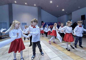 Taniec z białymi chustkami w parach na tle dekoracji.