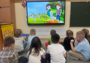 Dzieci siedzą i oglądają film edukacyjny.