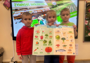 Dzieci pozują z planszą przedstawiającą witaminy A i B.