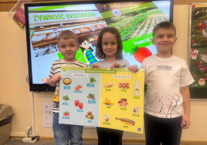 Dzieci pozują z planszą przedstawiającą witaminy C i D.