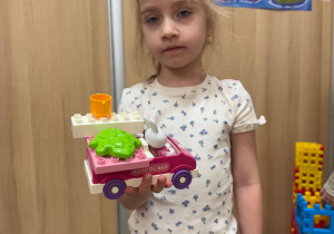 Dziewczynka pozuje z samochodem zbudowanym przez siebie.