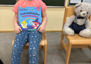 Dziewczynka siedzi obok misia ze swoją ulubioną książeczką.