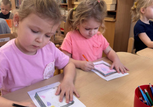 Dziewczynki siedzą przy stoliku i projektują okładki swoich książek.