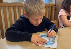 Chłopiec siedzi przy stoliku i projektuje okładkę swojej książki.