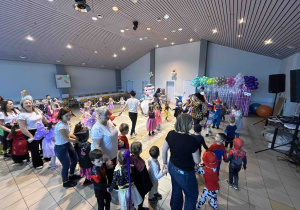 Przedszkolaki z paniami tańczą trzymając się za ręce.