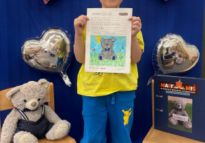 Chłopiec pozuje z Misiem i Dzienniczkiem Małego Misia podczas prezentacji swojej pracy.