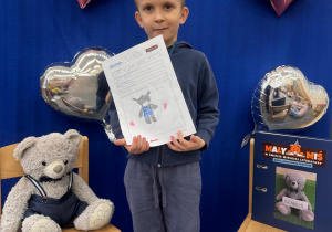 Chłopiec z dumą pokazuje swoją pracę plastyczną.