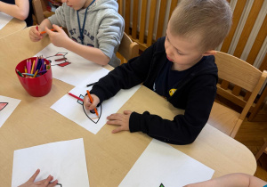 Dzieci siedzą przy stoliku i kolorują rakiety.