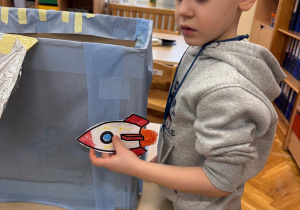 Chłopiec przykleja swoją kolorową rakietę do statku kosmicznego.