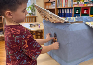 Chłopiec z zaangażowaniem ozdabia statek własnoręcznie wykonaną rakietą.