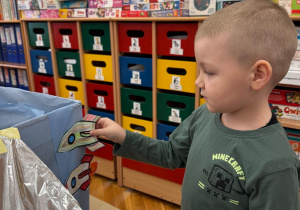 Chłopiec dokleja wyciętą i pokolorowaną rakietę do kosmicznej konstrukcji.