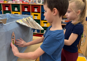 Chłopiec i dziewczynka przyklejają do statku kosmicznego swoje kolorowe rakiety.