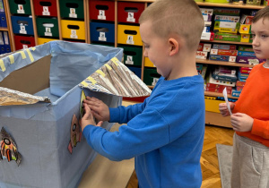 Chłopiec tworzy kosmiczną pracę plastyczną, umieszczając swoją rakietę na statku.