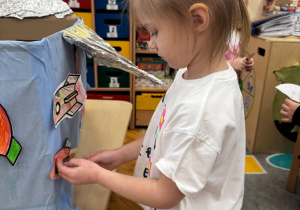 Dziewczynka przykleja swoją kolorową rakietę do statku kosmicznego.