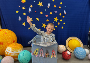 Chłopiec bawi się w kosmonautę, siedząc w pudełku udekorowanym rakietami.