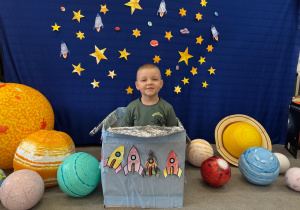 Chłopiec uczestniczy w kosmicznej zabawie, otoczony planetami i gwiazdami.