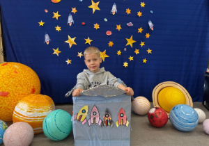 Chłopiec pozuję do zdjęcia na tle kosmicznej dekoracji z rakietami i planetami.