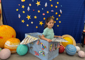 Dziewczynka z radością pozuję w pudełkowym statku kosmicznym podczas kosmicznych zajęć.