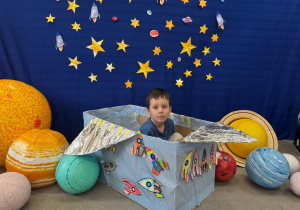 Chłopiec bawi się w kosmonautę, siedząc w pudełku udekorowanym rakietami.