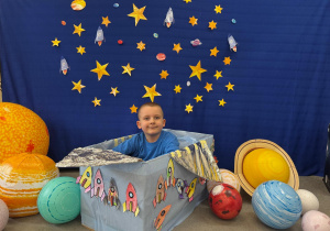 Chłopiec z uśmiechem „leci” w kosmos, siedząc w statku z pudełka.