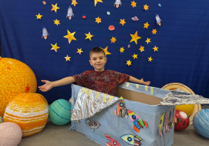 Chłopiec z uśmiechem „leci” w kosmos, siedząc w statku z pudełka.