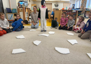 Dziewczynka przebrana za pingwinka czeka na polecenia dzieci, w którym kierunku ma się udać.