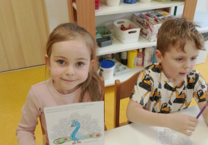 Dziewczynka pokazuje kolorowankę pawia.