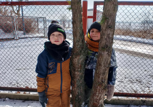 Chłopcy stoją koło drzewa.