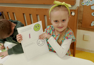 Dziewczynka pokazuje wypełnioną kartę pracy.