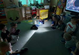 Chłopiec trzyma w ręku kartkę z planetami podświetloną latarką.