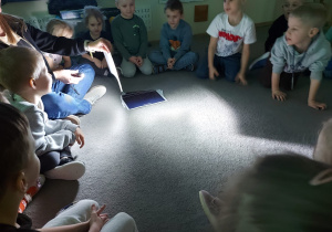 Dzieci siedzą w kole i oglądają obrazki dotyczące kosmosu.