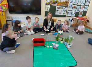 Dzieci siedza na dywanie i biorą udział w zajęciach