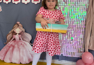 Dziewczynka pozuje z prezentami na tle ścianki.