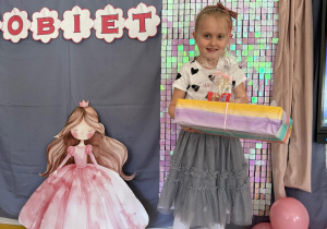 Dziewczynka pozuje z prezentami na tle ścianki.