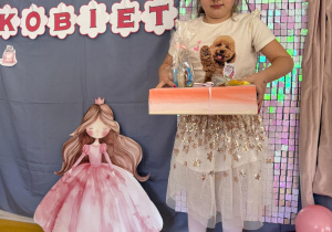 Dziewczynka pozuje z prezentami na tle ścianki.