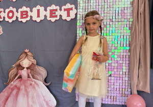 Dziewczynka pozuje z prezentami na tle ścianki.