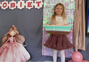 Dziewczynka pozuje z prezentami na tle ścianki.