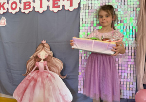 Dziewczynka z prezentami pozuje na tle ścianki.