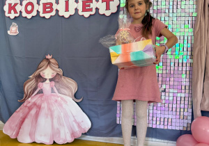 Dziewczynka z prezentami pozuje na tle ścianki.