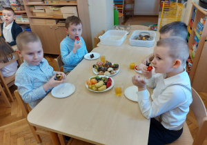 Chłopcy siedzą przy stoliku i spożywają poczęstune przygotowany przez rodziców.