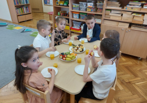 Dzieci siedzą przy stoliku i spożywają poczęstunek.