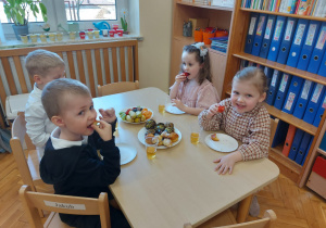 Dzieci siedzą przy stoliku i jedzą owoce.