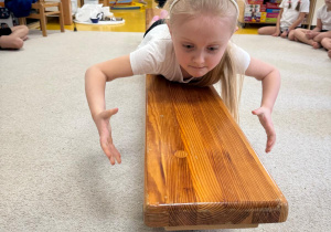 Dziewczynka przeciąga się po ławeczce.