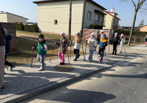 Uśmiechnięte dzieci maszerują z kijkami.